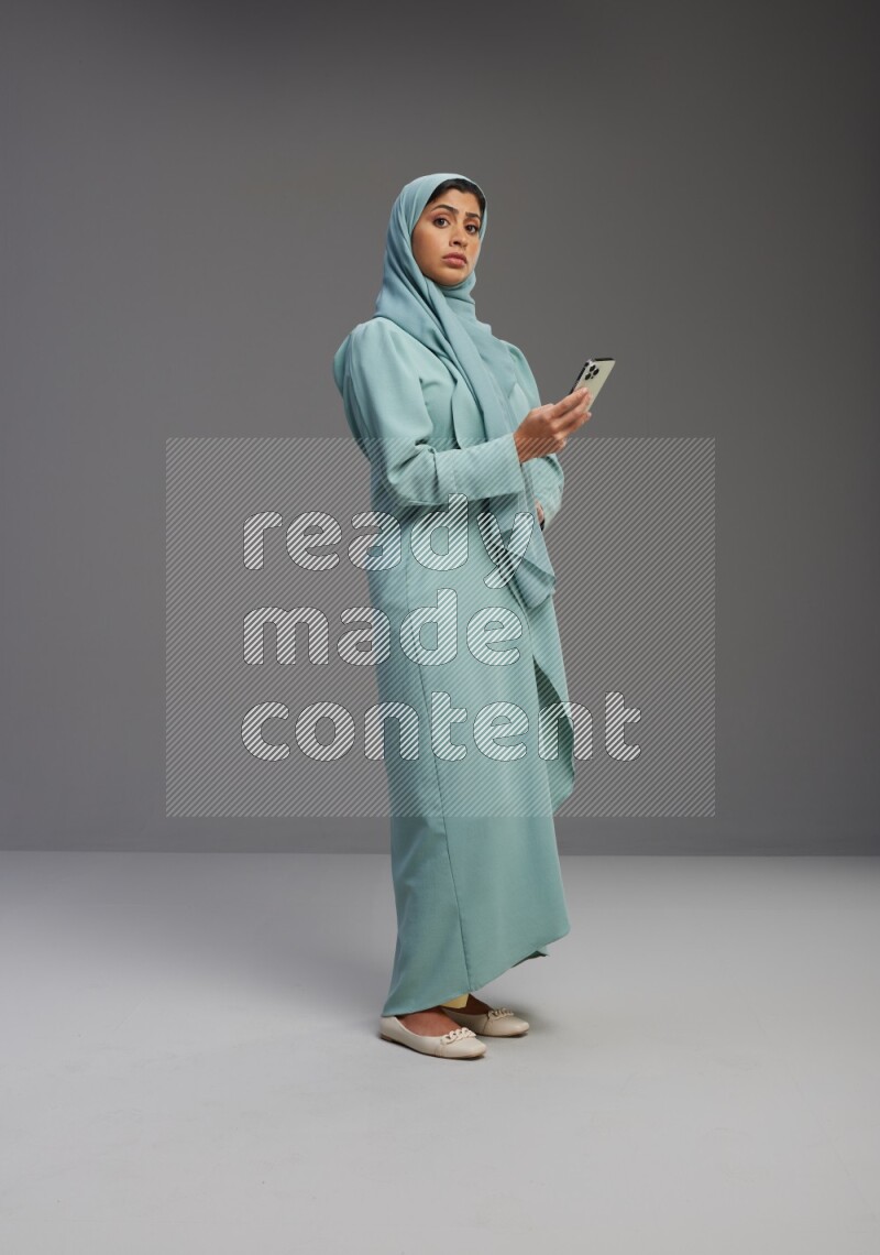 Saudi Woman wearing Abaya standing texting on phone on Gray background