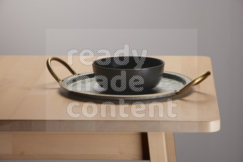 black bowl placed on a rounded stainless steel tray with golden handels on the edge of wooden table