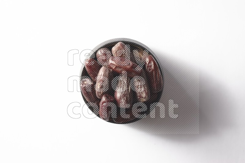 Dates in a black pottery bowl on white background