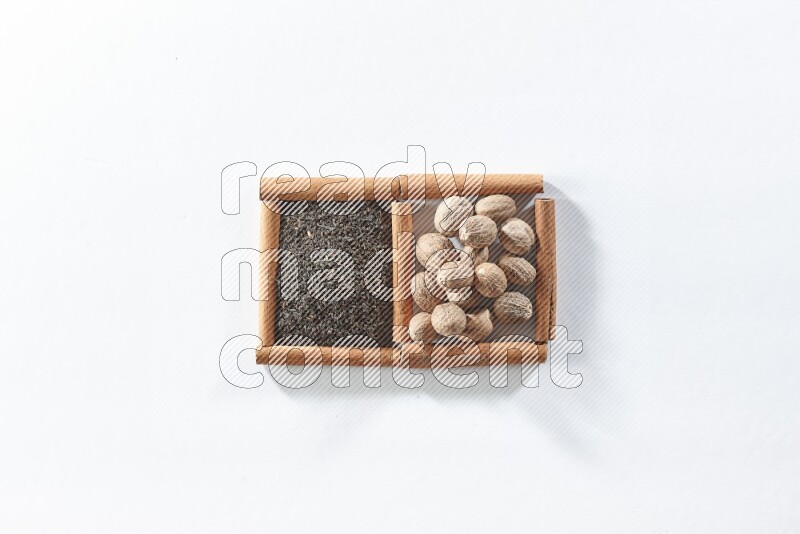 مربعان من أعواد القرفة ممتلئان بالشاي الأسود وجوزة الطيب علي خلفية بيضاء