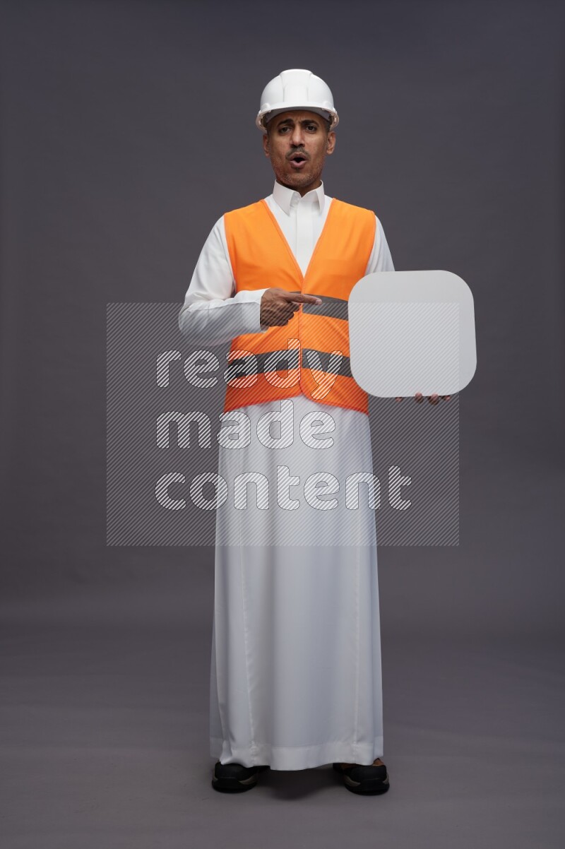 Saudi man wearing thob with engineer vest standing holding social media sign on gray background
