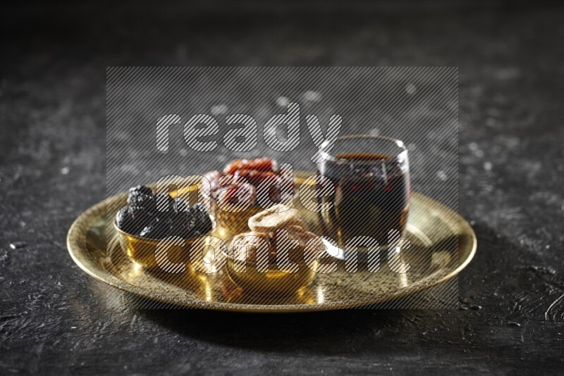 Dried fruits in metal bowls with tamarind on a tray in dark setup