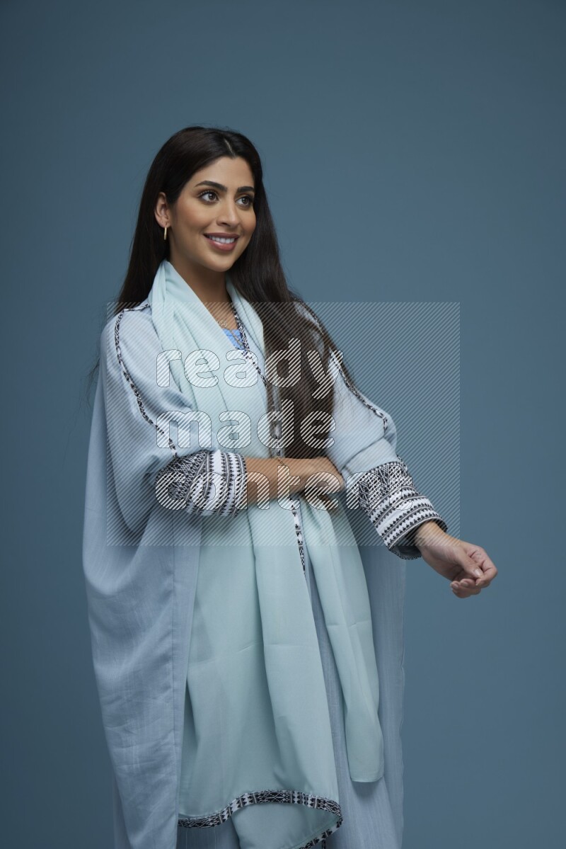 A woman posing in a blue background wearing blue Abaya no Hijab