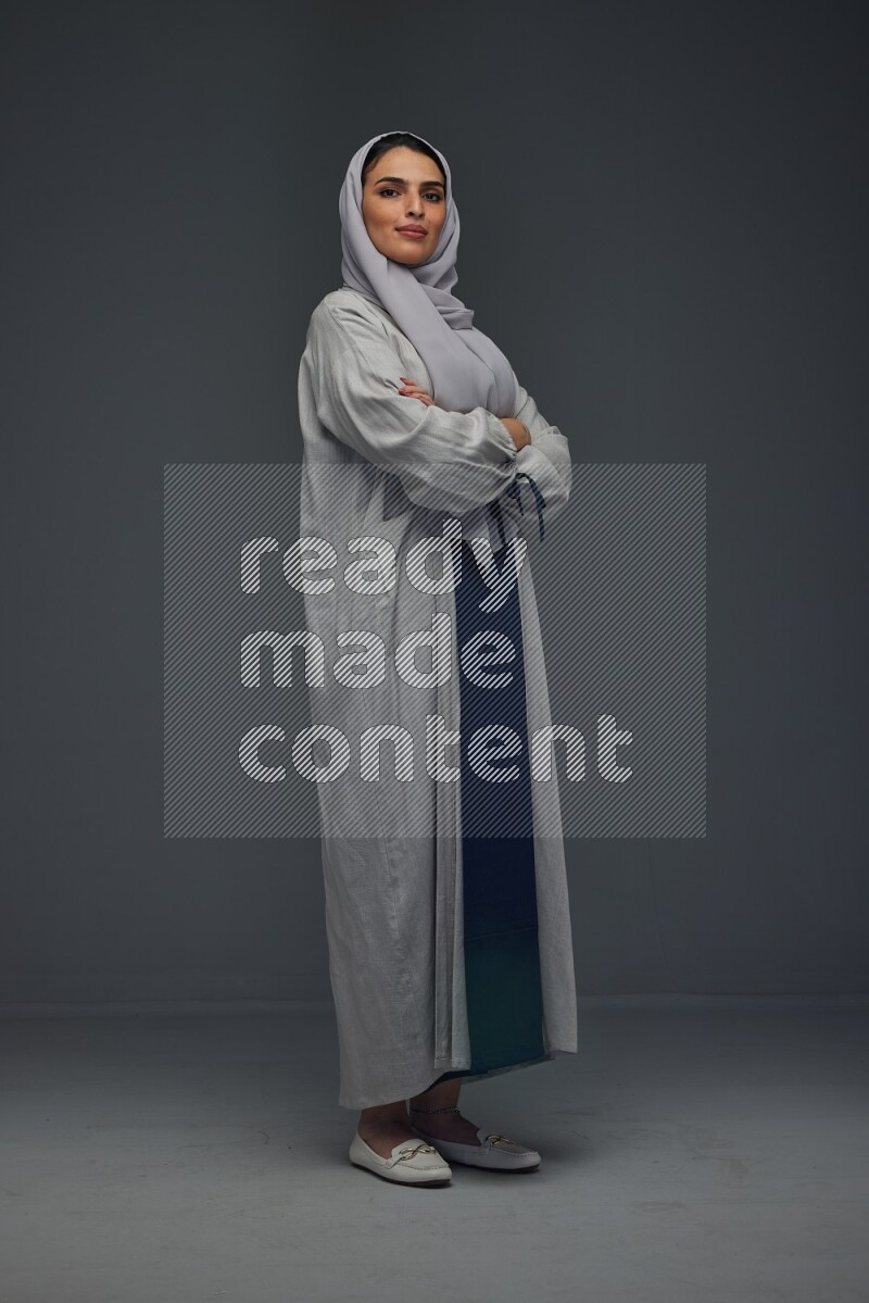 A Saudi woman wearing a light gray Abaya and head scarf standing and making multi poses eye level on a grey background