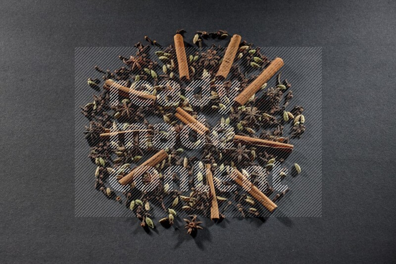Cardamom, star anise, cloves and cinnamon sticks on black flooring