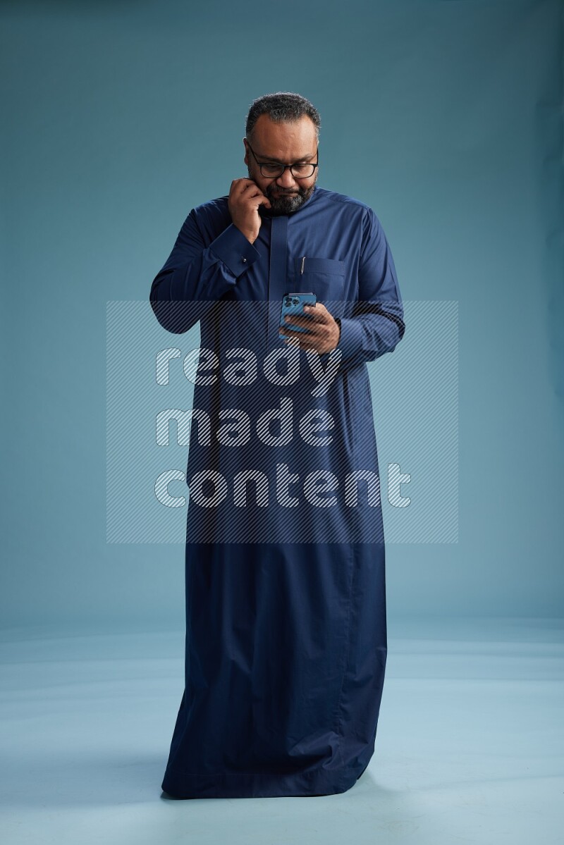 Saudi Man without shimag Standing texting on phone on blue background