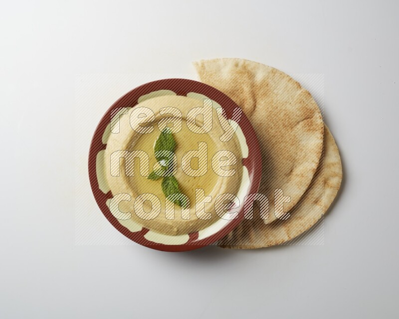 Hummus in a traditional plate garnished with mint on a white background
