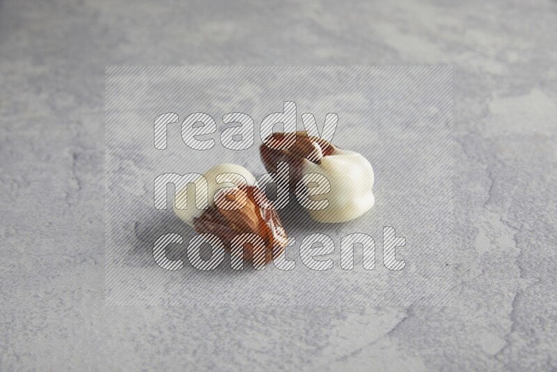 two almonds stuffed dates covered with white chololate on a light grey background