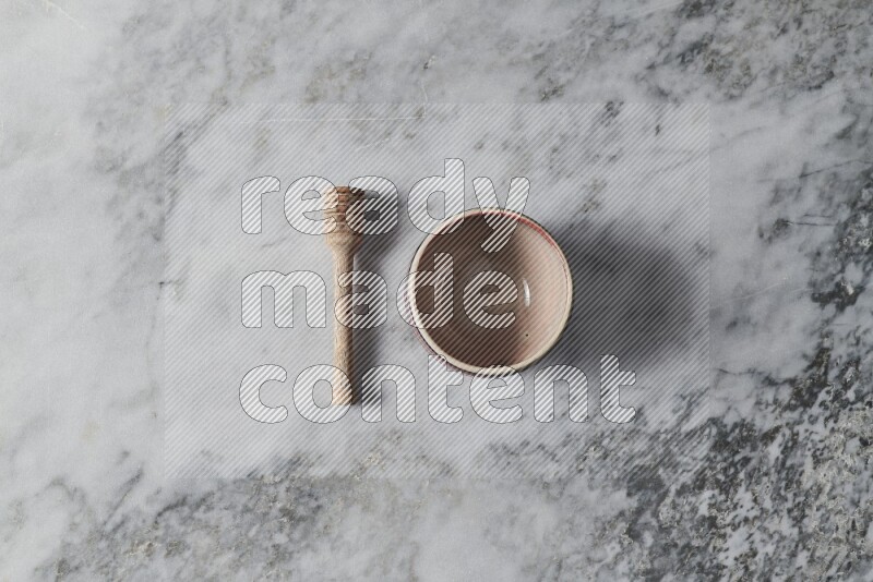 Multicolored pottery bowl with wooden honey dipper on the side on grey marble background