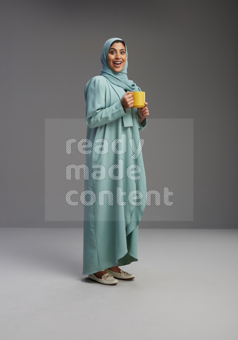 Saudi Woman wearing Abaya standing  holding a mug on Gray background