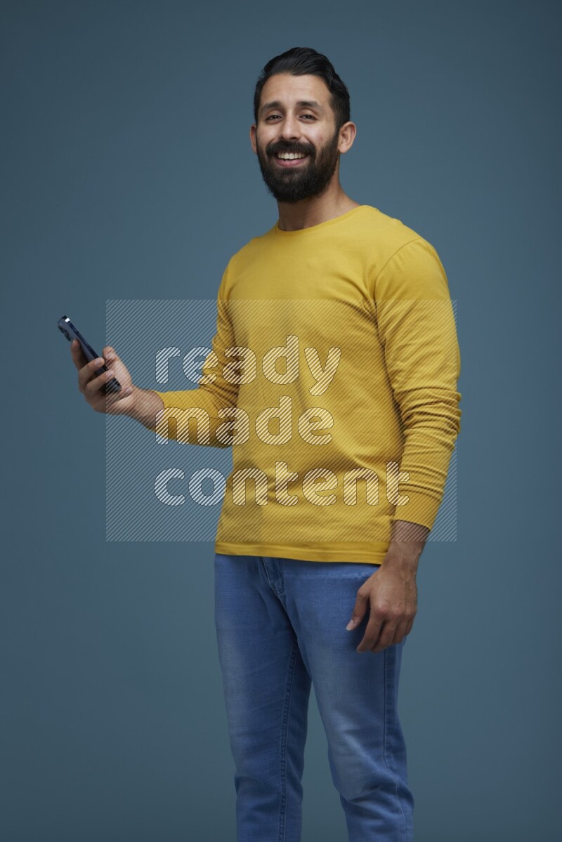 Man posing with a phone in a blue background wearing a yellow shirt
