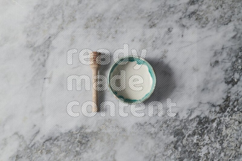 Multicolored pottery bowl with wooden honey dipper on the side on grey marble background