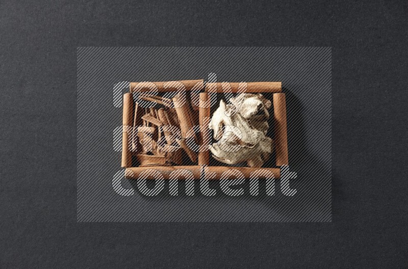 مربعان من أعواد القرفة ممتلئان بقطع من القرفة والزنجبيل المجفف علي خلفية سوداء