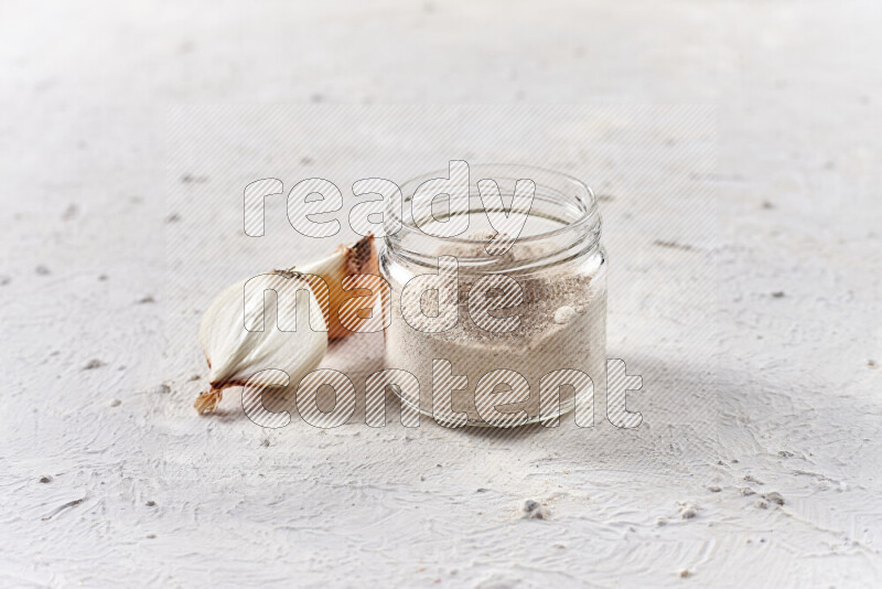 A glass jar full of onion powder on white background