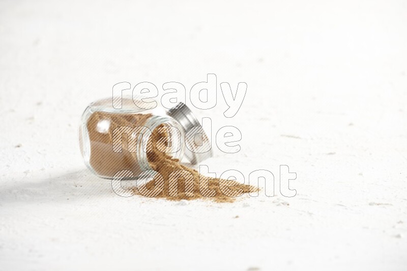 Flipped glass jar full of cinnamon powder on a textured white background