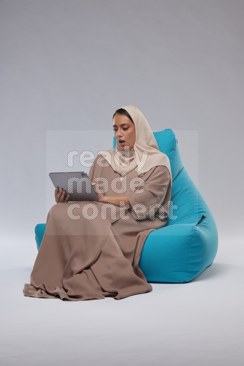 A Saudi woman sitting on a blue beanbag and working on tablet