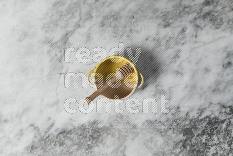 Multicolored pottery bowl with wooden honey dipper in it on grey marble background