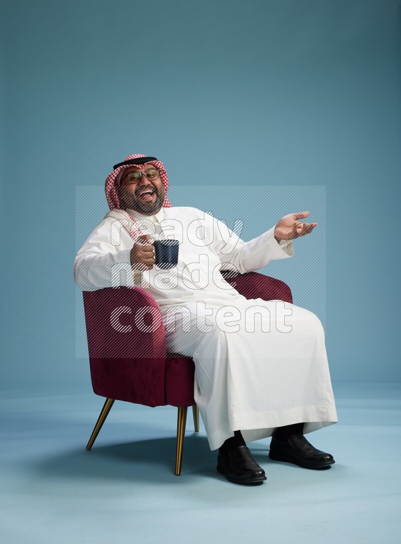 Saudi Man with shimag sitting on chair drinking coffee on blue background
