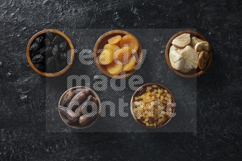 Dried fruits in wooden bowls in a dark setup