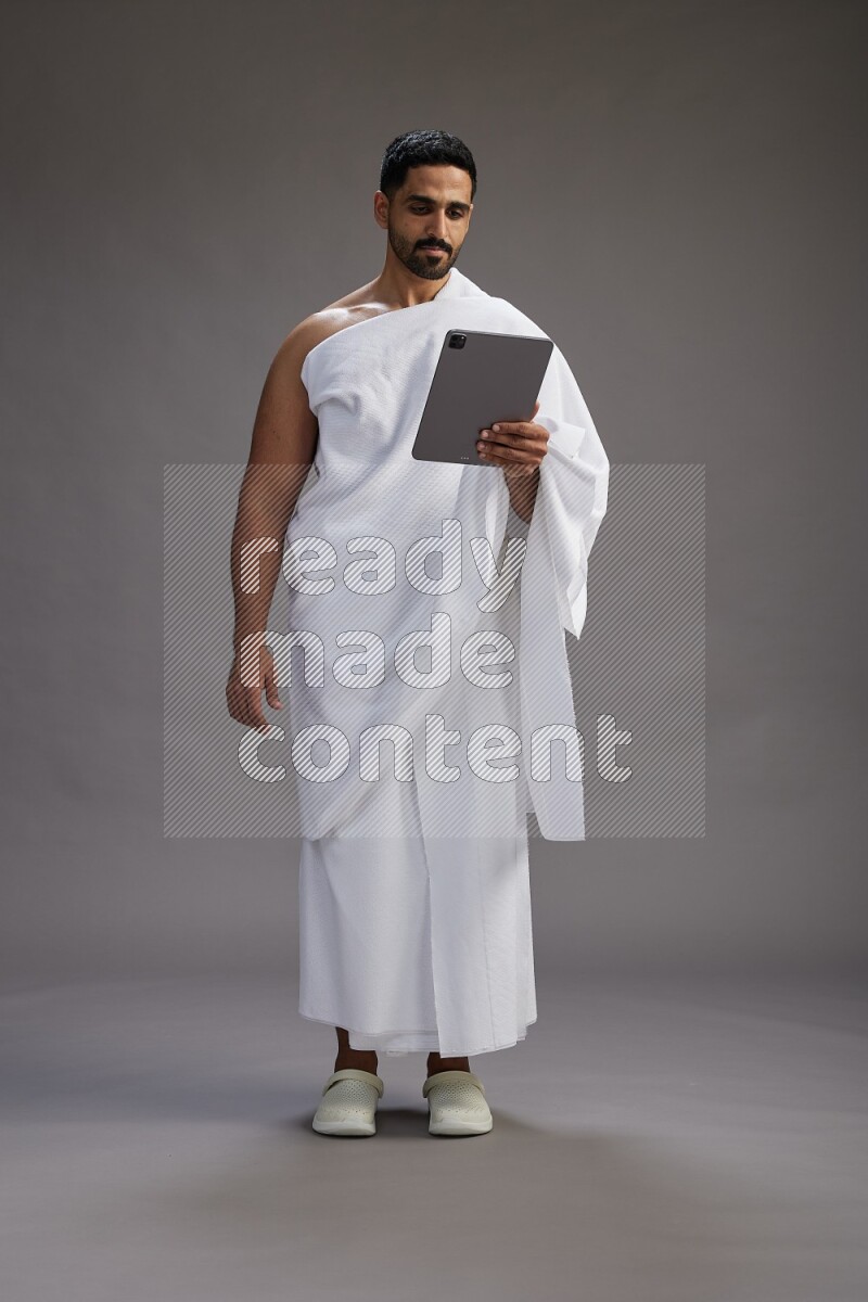 A man wearing Ehram and holding a tablet on gray background