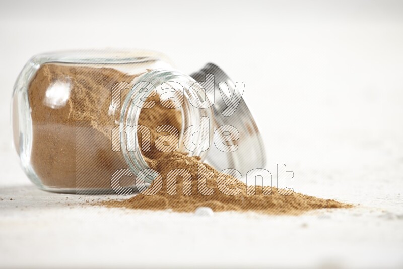 Flipped glass jar full of cinnamon powder on a textured white background