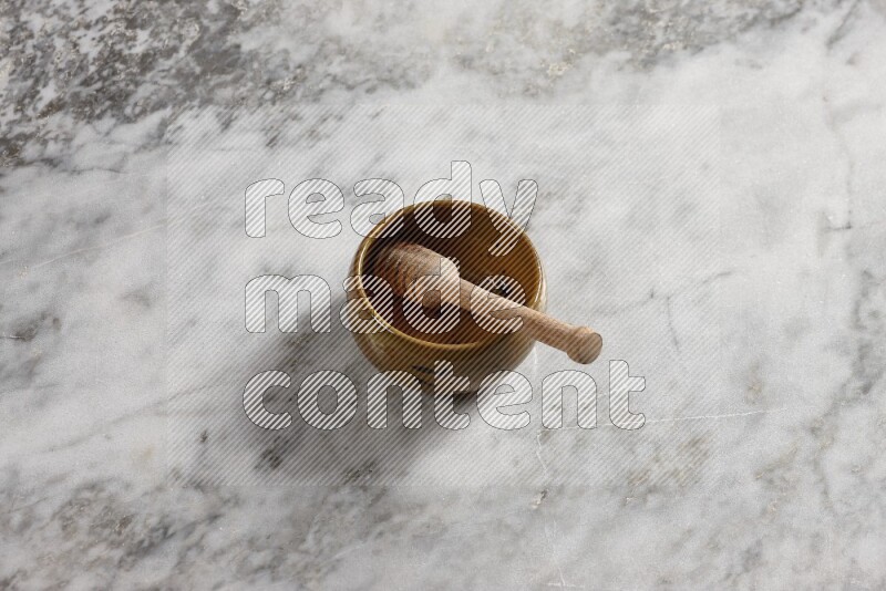 Multicolored pottery bowl with wooden honey dipper in it on grey marble background