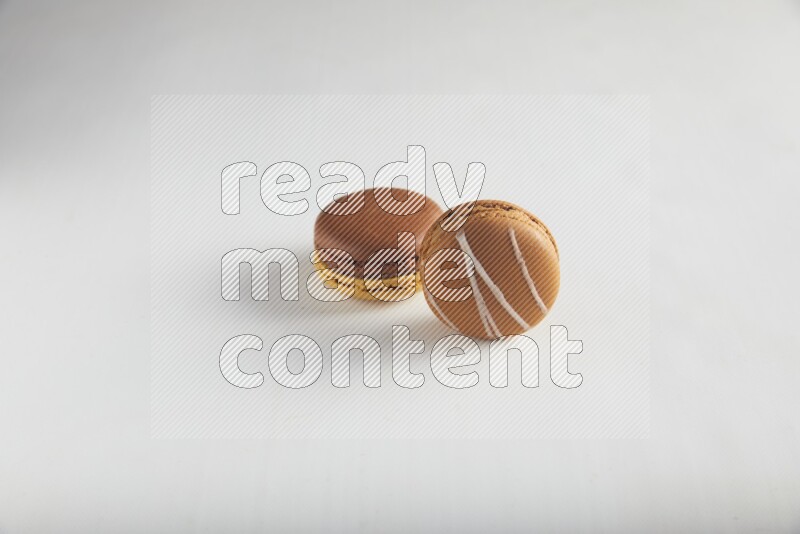45º Shot of of two assorted Brown Irish Cream, and Yellow, and Brown Chai Latte macarons on white background