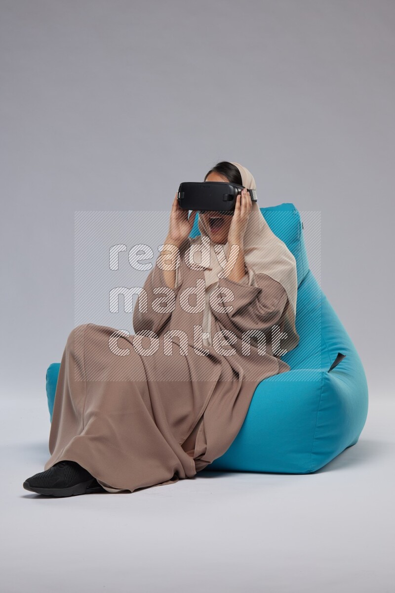 A Saudi woman sitting on a blue beanbag and gaming with VR