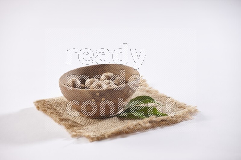 A wooden bowl full of whole nutmeg seeds on burlap fabric on a white flooring