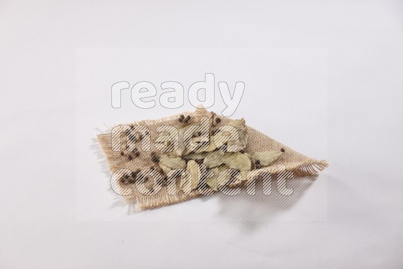 Dried bay leaves and allspice berries on a piece of burlap on white flooring in different angles