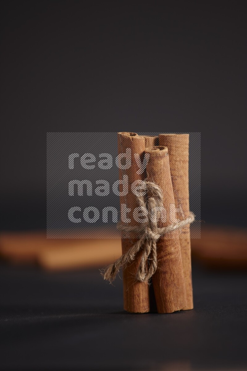 4 Cinnamon sticks stacked and bounded with more sticks in the background on black flooring