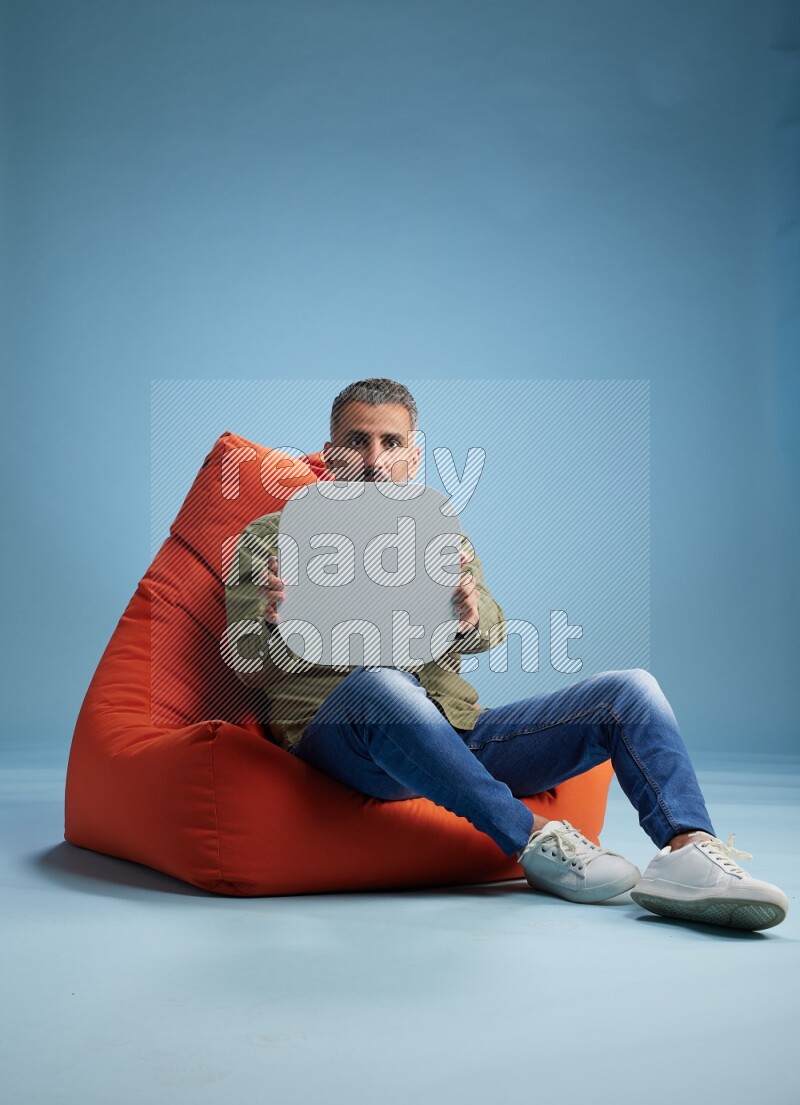 A man sitting on a orange beanbag and holding social media sign