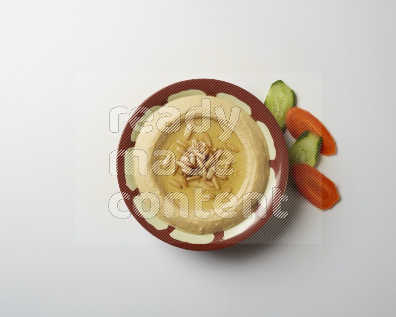 Hummus in a traditional plate garnished with pine nuts on a white background