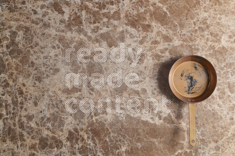 A small copper pan on beige marble background