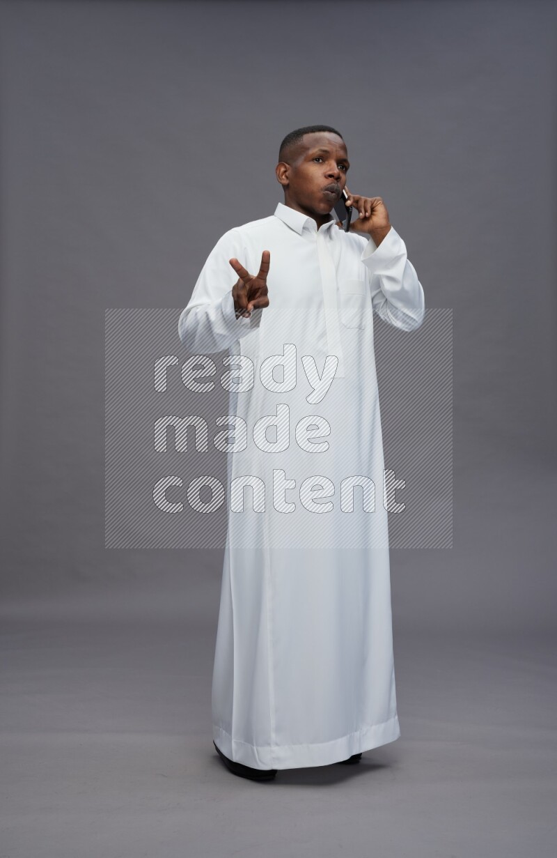 Saudi man wearing thob standing talking on phone on gray background