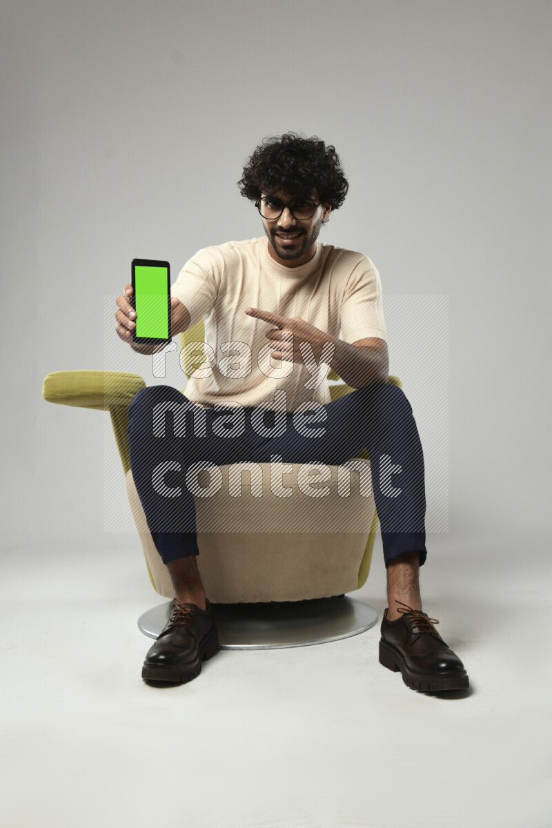 A man wearing casual sitting on a chair showing a phone screen on white background
