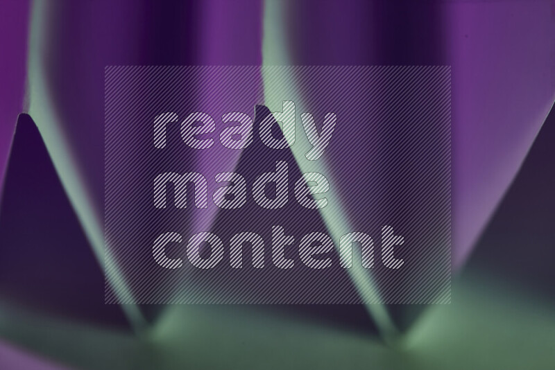 صورة مجردة مقربة تظهر طيات ورقية هندسية حادة بتدرجات اللون الأخضر والارجواني