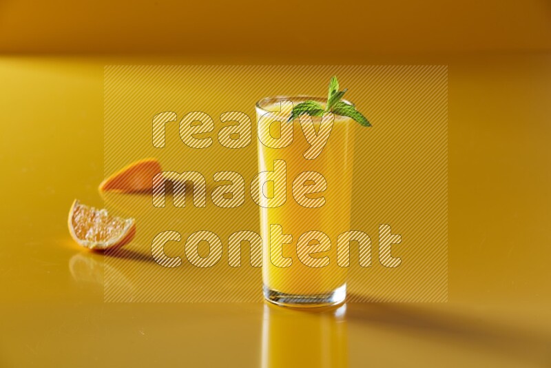 glass of orange juice with  mint on yellow background
