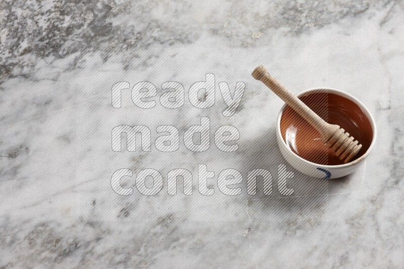 Multicolored pottery bowl with wooden honey dipper in it on grey marble background