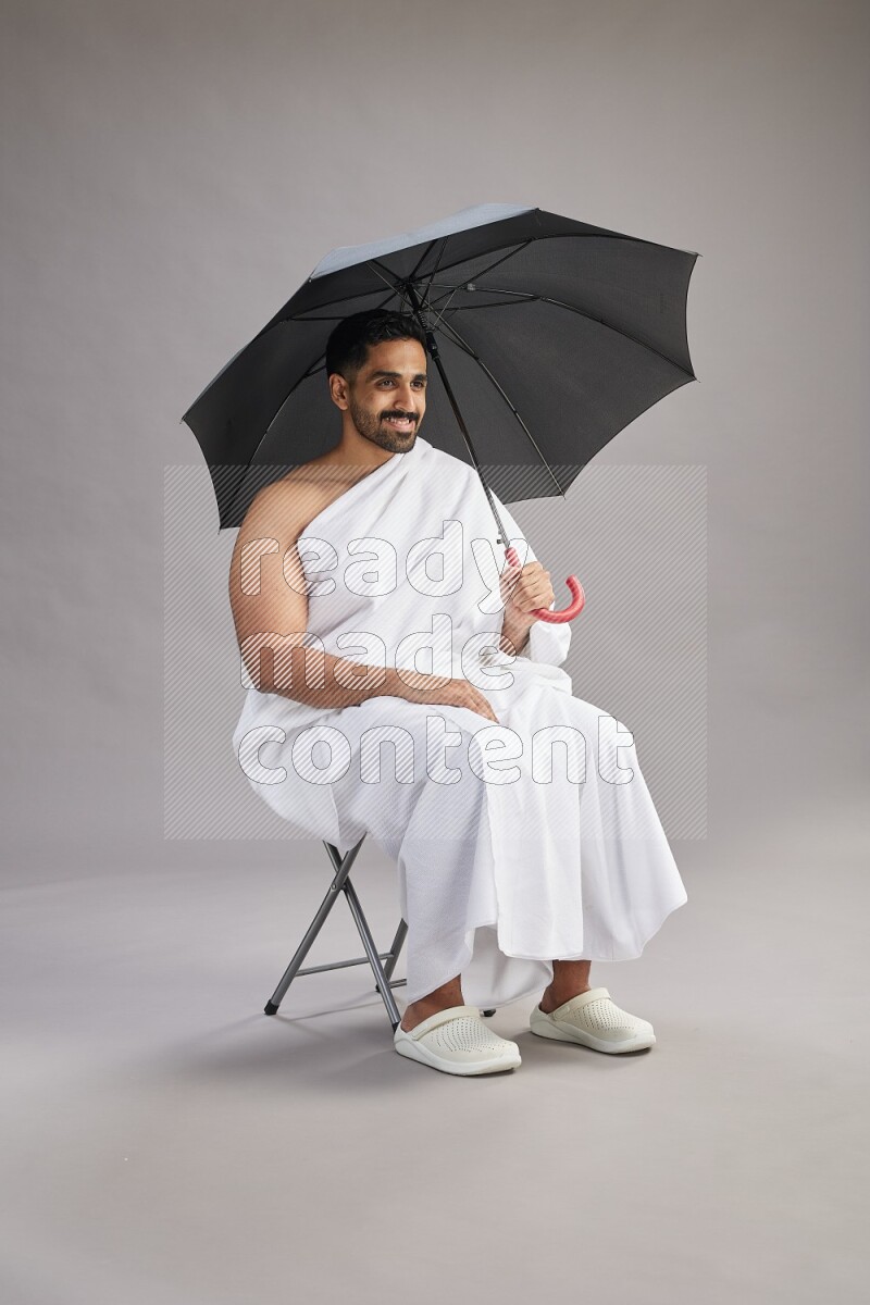 A man wearing Ehram with face mask Standing holding umbrella on gray background