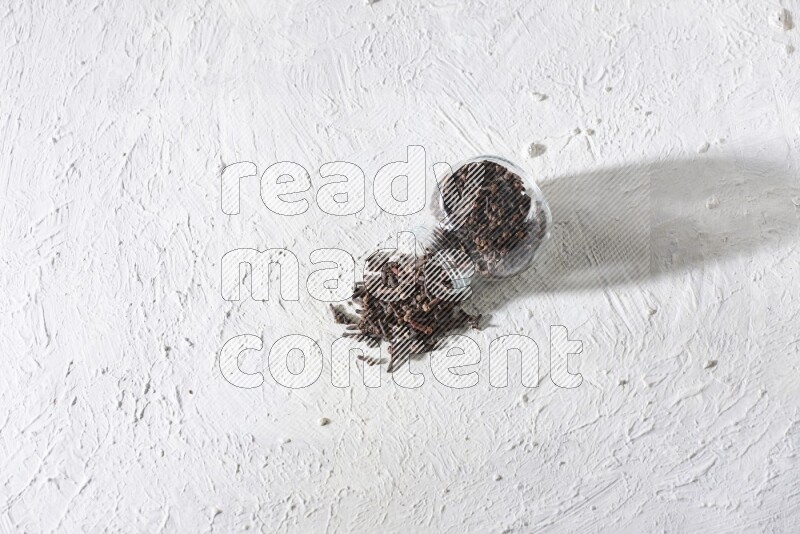 وعاء زجاجي مقلوب ممتلئ بالقرنفل وتناثر القرنفل منه على أرضية بيضاء