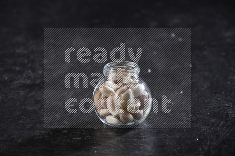 A glass spice jar full of garlic cloves on a textured black flooring