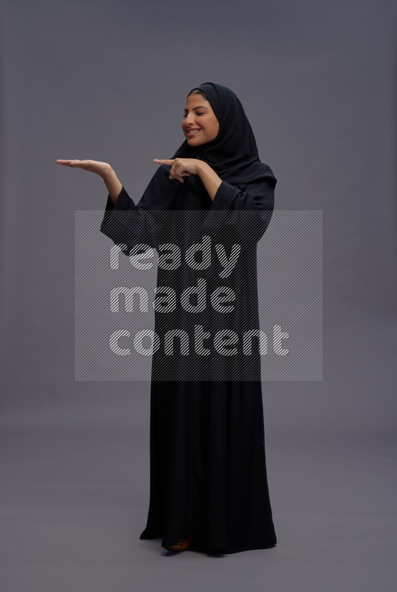 Saudi woman wearing Abaya standing interacting with the camera on gray background