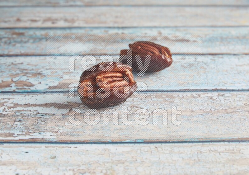 two pecan stuffed madjoul dates on a light blue wooden background