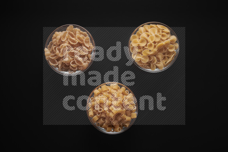 Different pasta types in glass bowls on black background