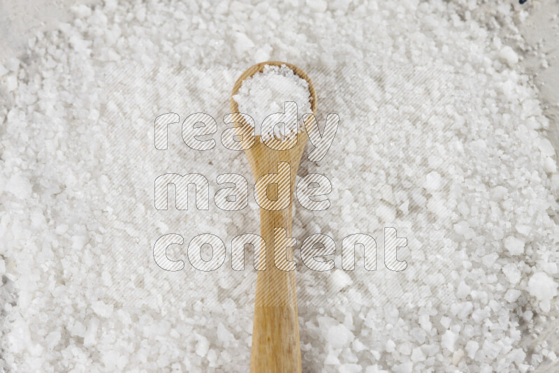 A wooden spoon full of white salt on white background