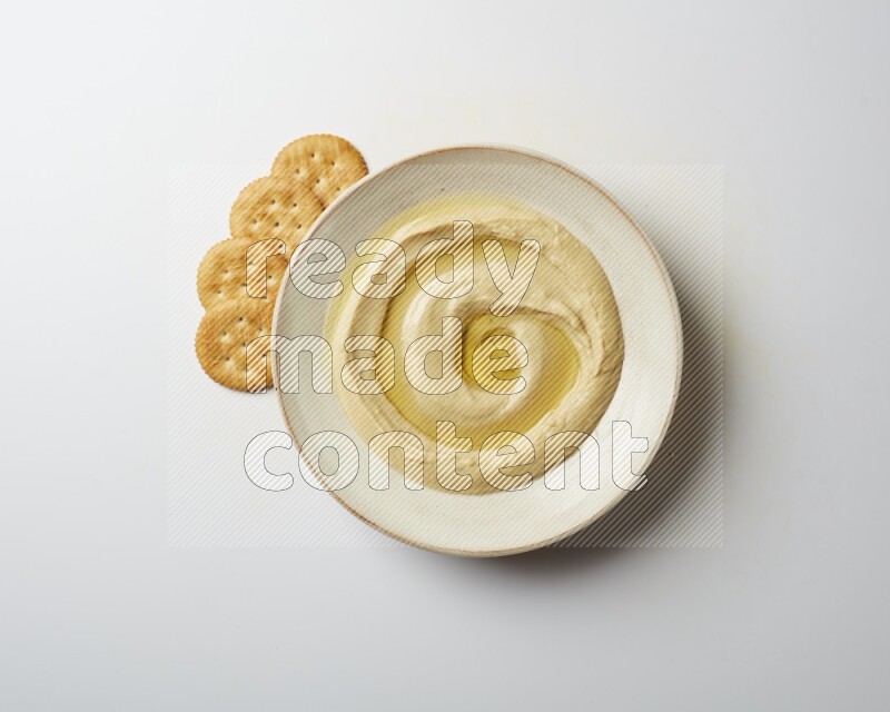 Hummus in a pottry plate garnished with olive oil on a white background