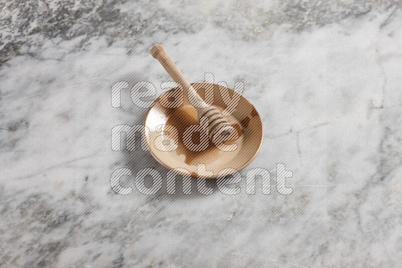 Multicolored pottery plate with wooden honey dipper in it on grey marble background