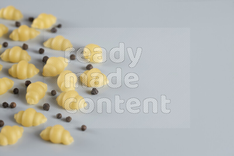 Raw pasta with different ingredients such as cherry tomatoes, garlic, onions, red chilis, black pepper, white pepper, bay laurel leaves, rosemary, cardamom and mushrooms on light blue background