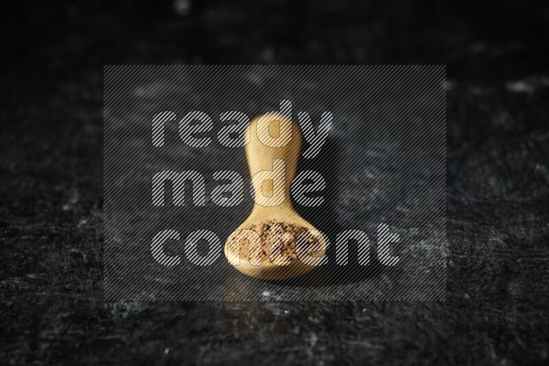 A wooden spoon full of allspice powder on a textured black flooring